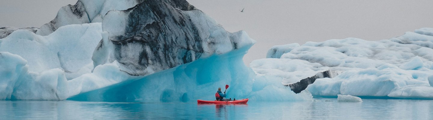 person kayaking next to glacier